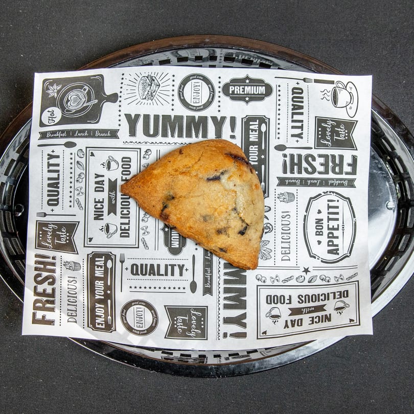 Triangular blueberry scone on a black and white patterned paper liner in a dark serving tray.