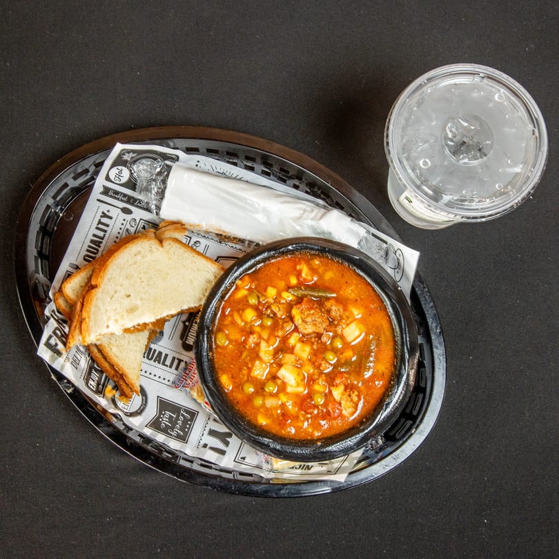 Hearty stew with bread slices and a drink served in a black basket.