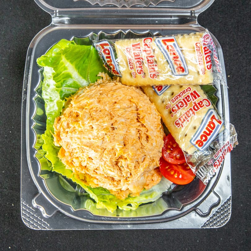 Scoop of chicken salad, lettuce, sliced tomatoes, and Lance Captain's Wafers in a clear takeout container.