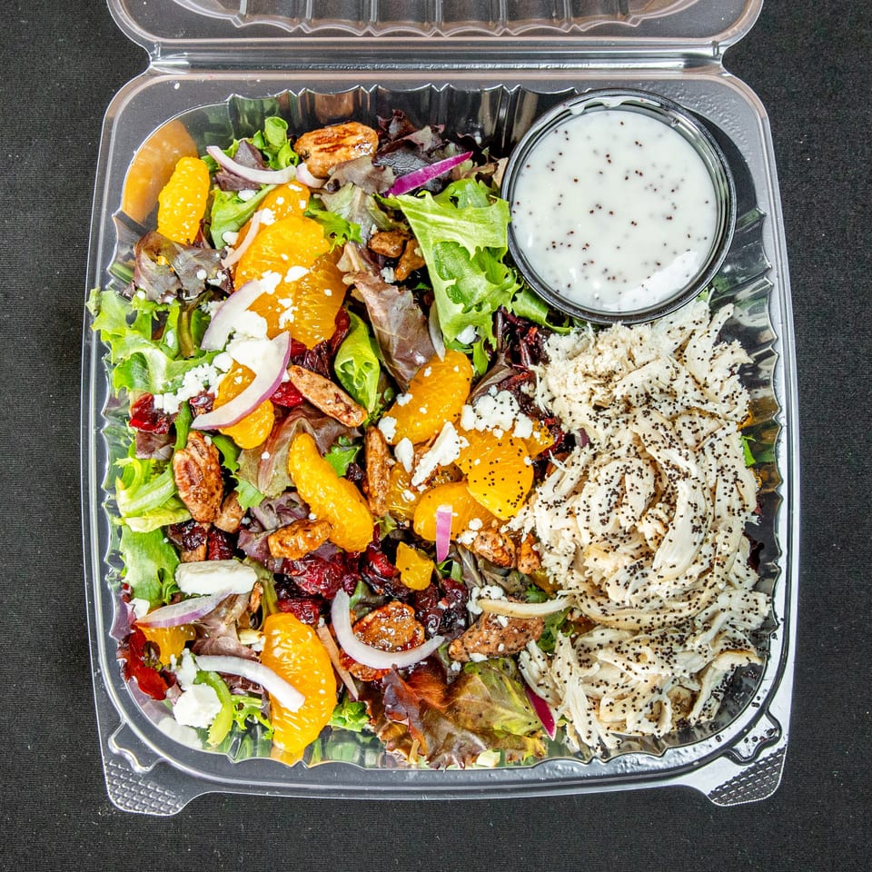 Chicken salad with oranges, pecans, cranberries, feta, and dressing in a clear to-go container.