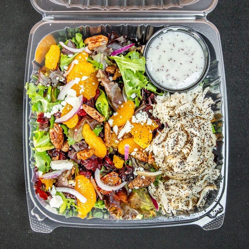 Chicken salad with oranges, pecans, cranberries, feta, and dressing in a clear to-go container.