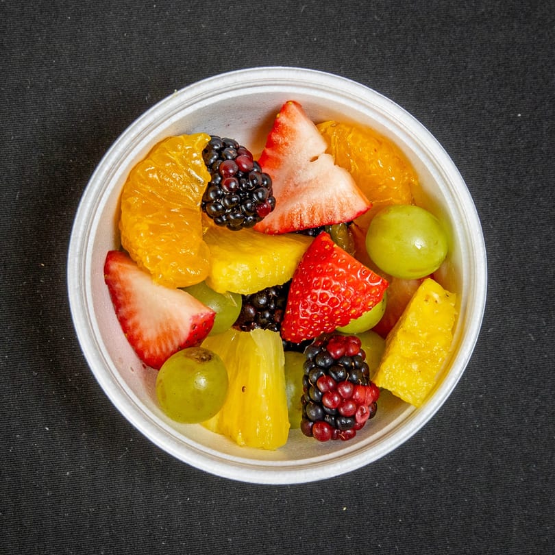 Colorful fruit cup with strawberries, green grapes, blackberries, pineapple, and orange segments.